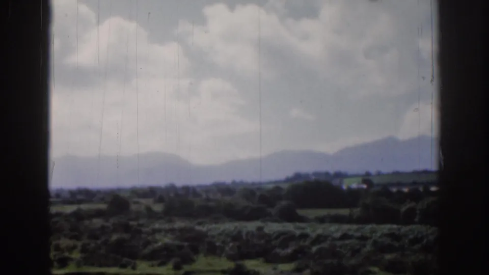 Dublin, Ireland 1961 landscape frame showing fields, tree lines, distant mountains, and soft clouds in faded 8mm color.