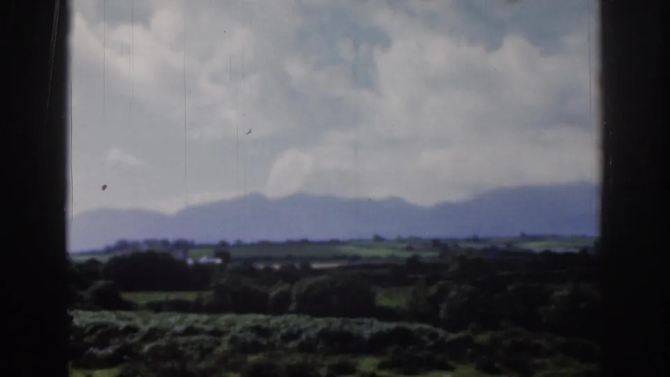 Dublin, Ireland 1961 countryside view with a green valley, distant hills, pale clouded sky, and visible 8mm film wear.