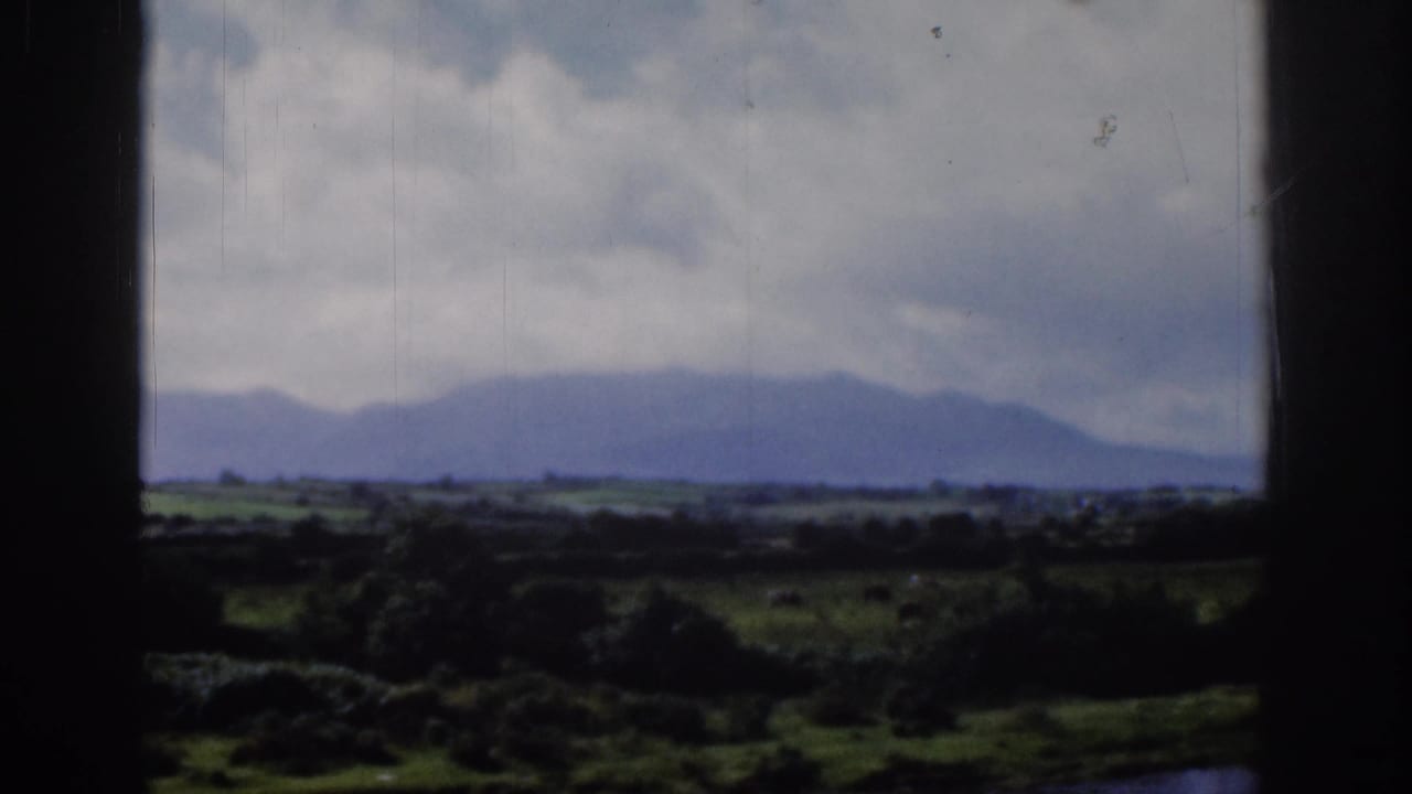 1961 Dublin-area home-movie view of a distant mountain silhouette, cloudy sky, and green fields framed by a dark window.