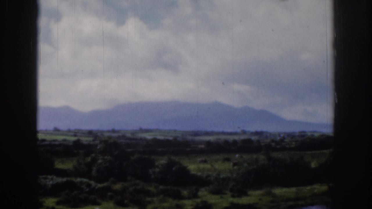 1961 Ireland countryside view through a window, with distant blue-gray mountains, low fields, and a cloudy sky.