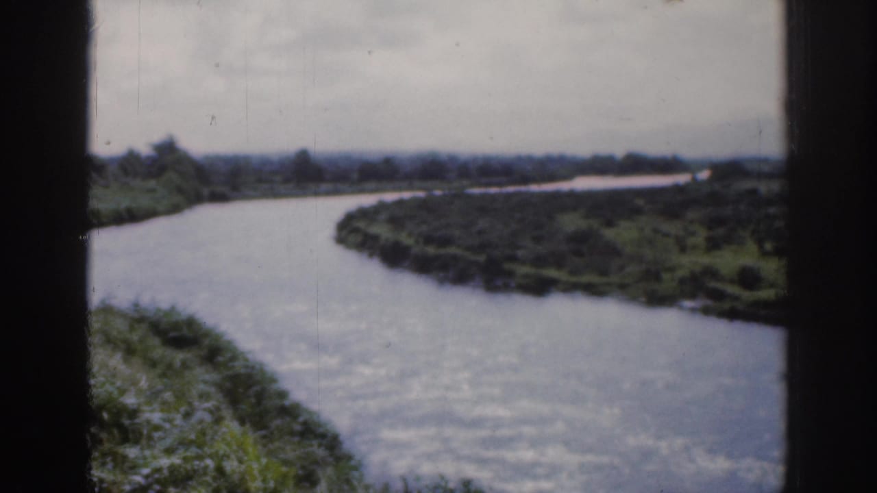 1961 Dublin home-movie frame showing a broad winding river or canal with green banks and distant low horizon.