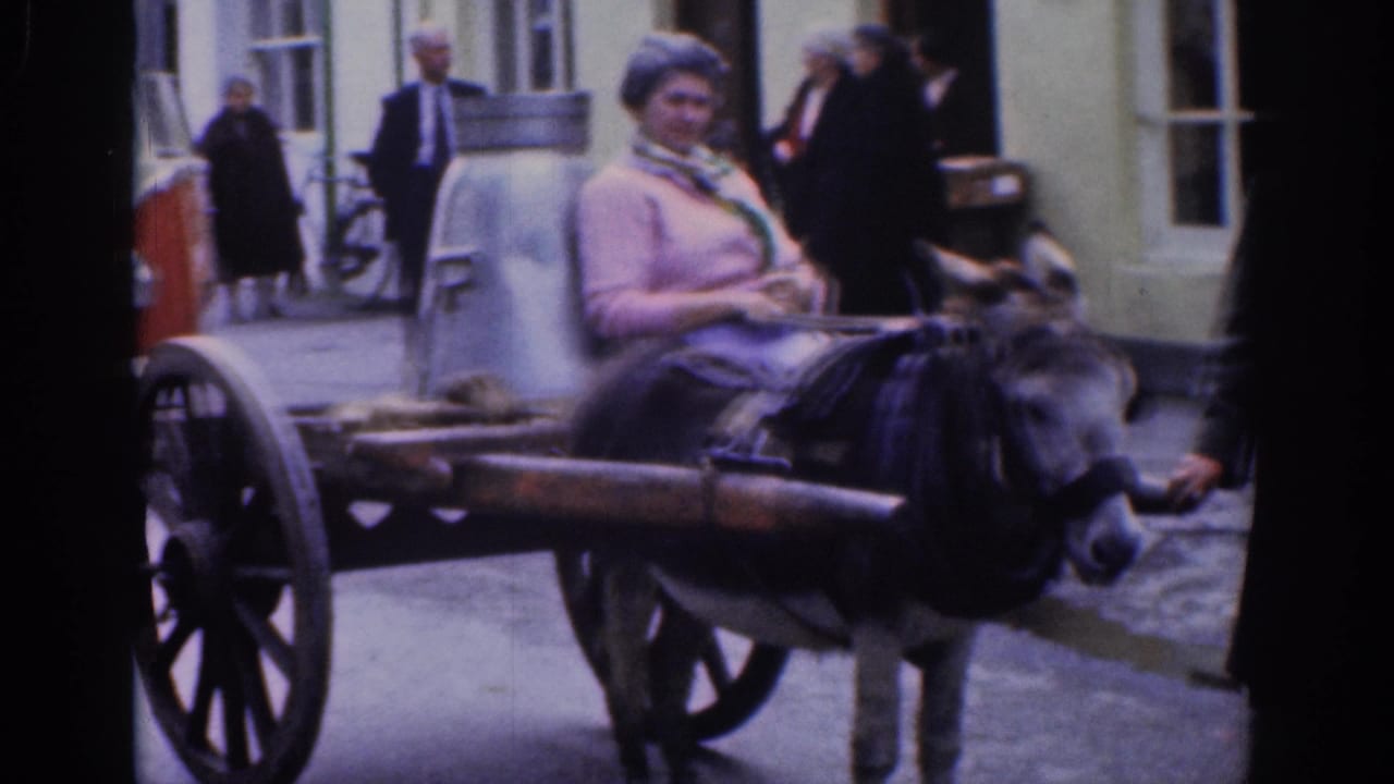 1961 Dublin street scene with a woman in a pink sweater riding a donkey-drawn cart past pedestrians and building fronts.