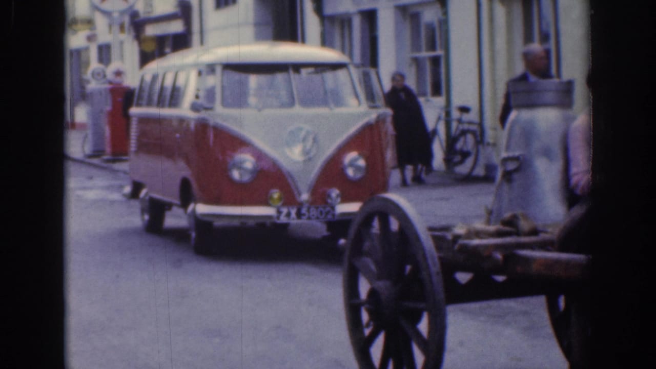 Red and white Volkswagen van approaches on the street beside part of a cart.