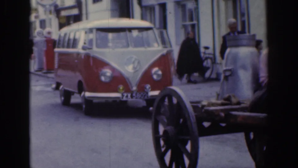 1961 Dublin street view with a red and white Volkswagen van passing a donkey cart, pedestrians, bicycles, and storefronts.
