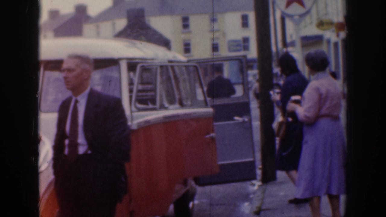 Man in suit beside a two-tone van with pedestrians on the street.