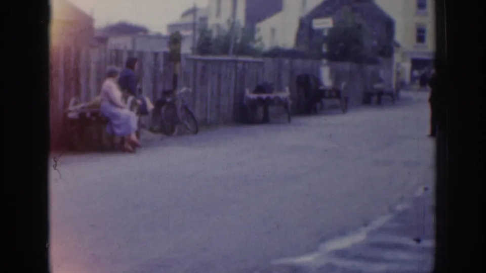 Wider Dublin street view with people seated by a wooden fence, bicycles nearby, benches, and pedestrians in the distance.