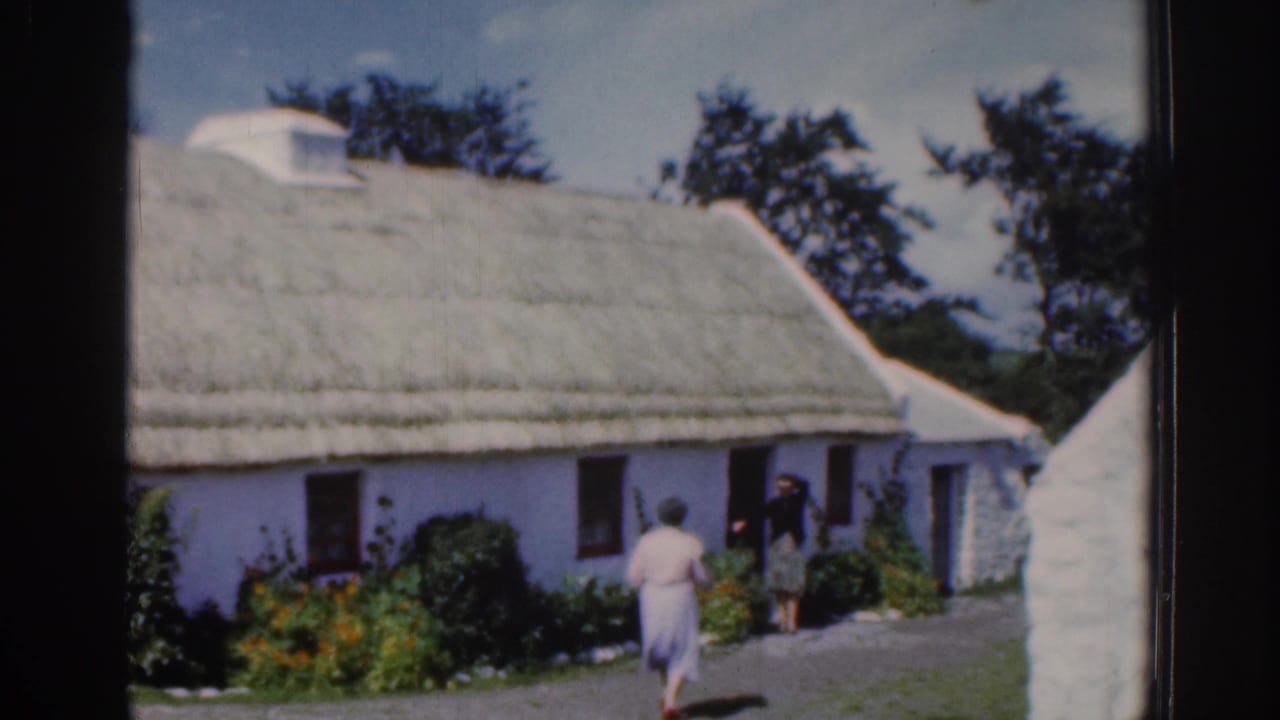 White thatched cottage with a woman walking toward figures near the doorway.