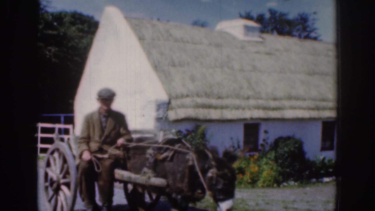 1961 Dublin-area footage shows a man seated on a wooden mule-drawn cart passing a white thatched cottage and gate.