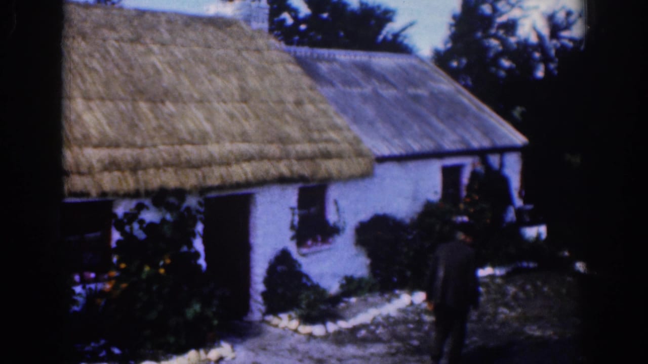 Man in dark clothing near the doorway of a white cottage with a thatched roof.