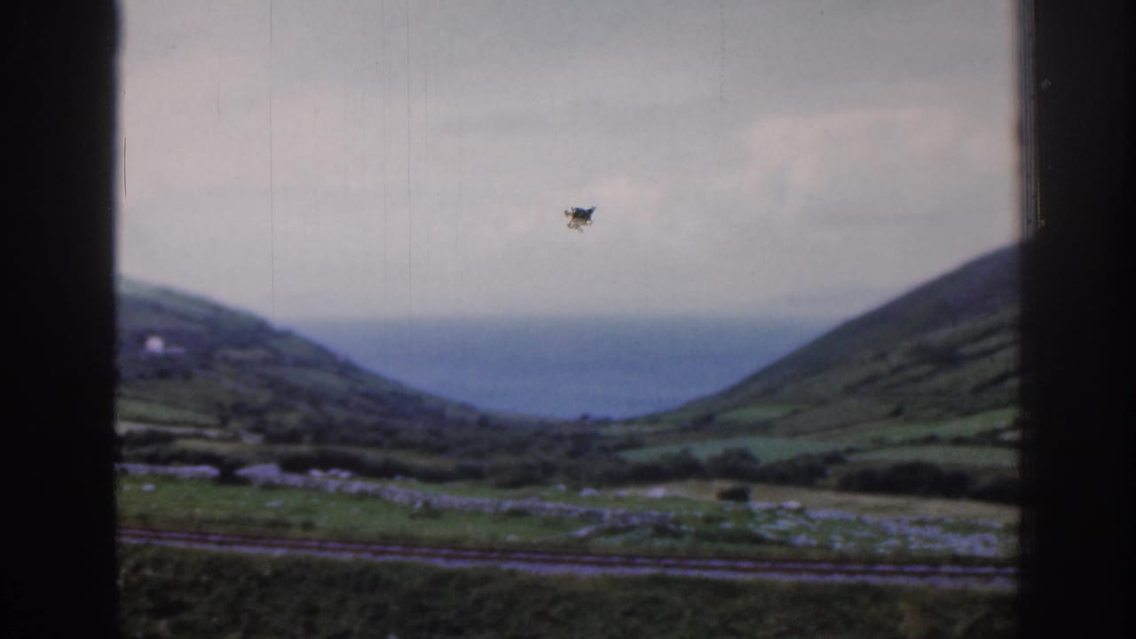 Rolling hills and a distant body of water framed by dark vertical train-window bars.