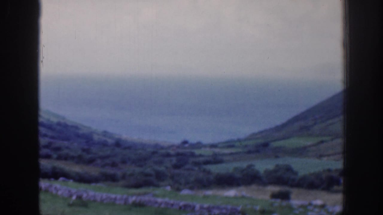 1961 Ireland 8mm view of green hillside fields and the ocean horizon through a dark window frame.