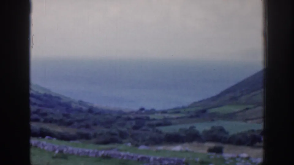 1961 Ireland 8mm view of green hillside fields and the ocean horizon through a dark window frame.