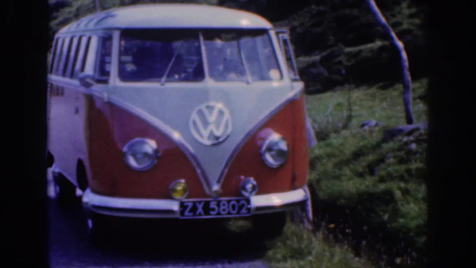 1961 Ireland frame showing a red and white Volkswagen Type 2 van parked on a narrow country road beside grassy verges.