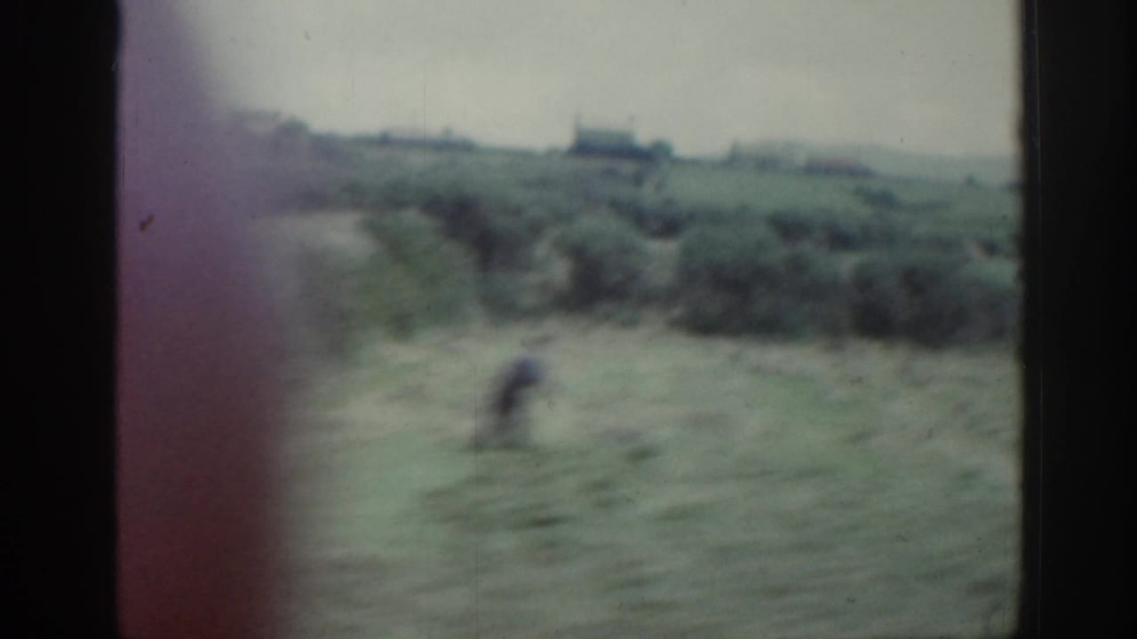 Soft 8mm view of rural Ireland with a blurred person crossing a field below distant buildings.
