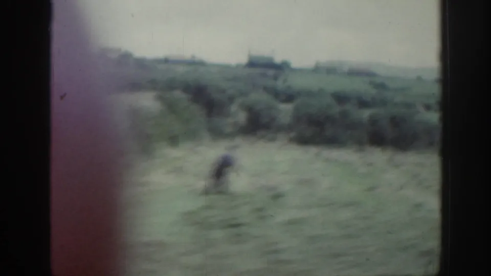 Soft 8mm view of rural Ireland with a blurred person crossing a field below distant buildings.