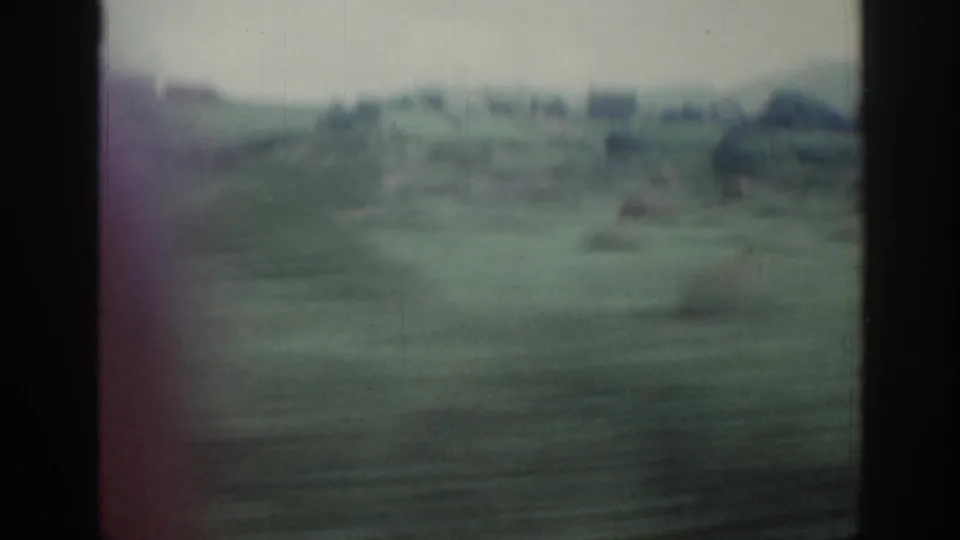 1961 Ireland 8mm frame showing blurred fields and distant low buildings through dark train-window bars.