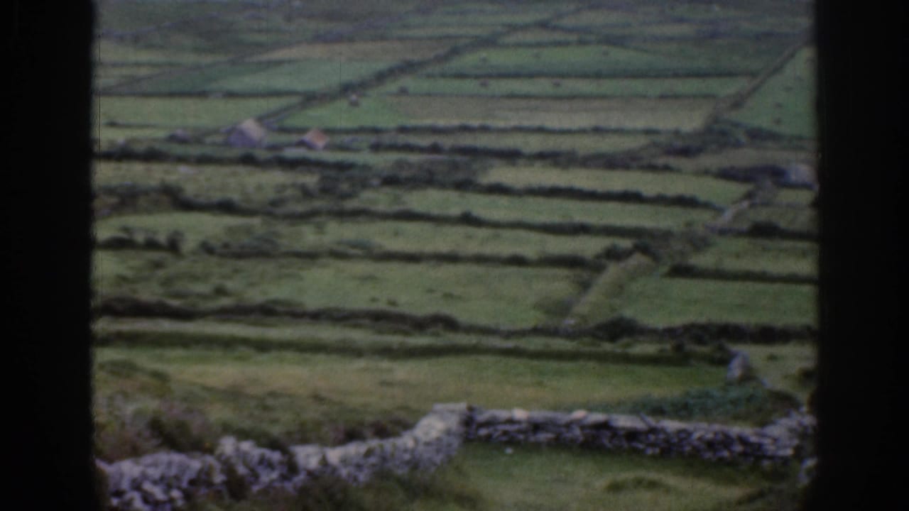 Patchwork green fields and stone walls with a dark vertical frame in the foreground.
