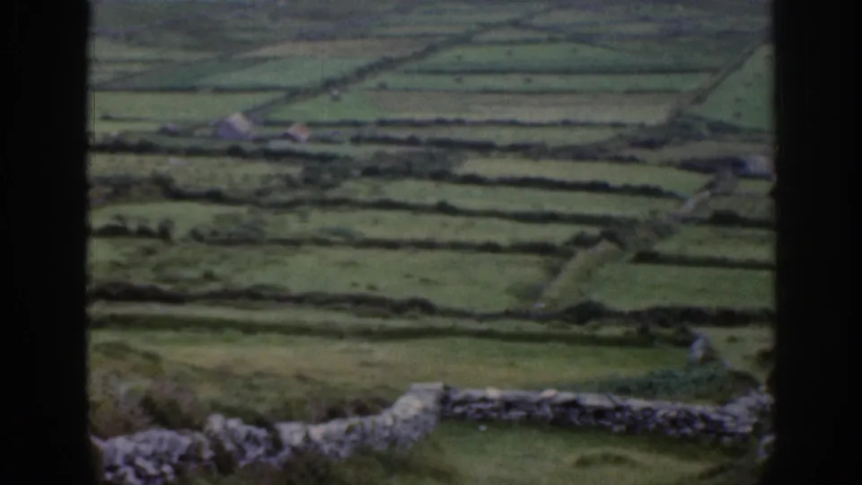 Rural Irish field pattern with stone walls, small structures, and a dark vertical window or frame edge in the foreground.