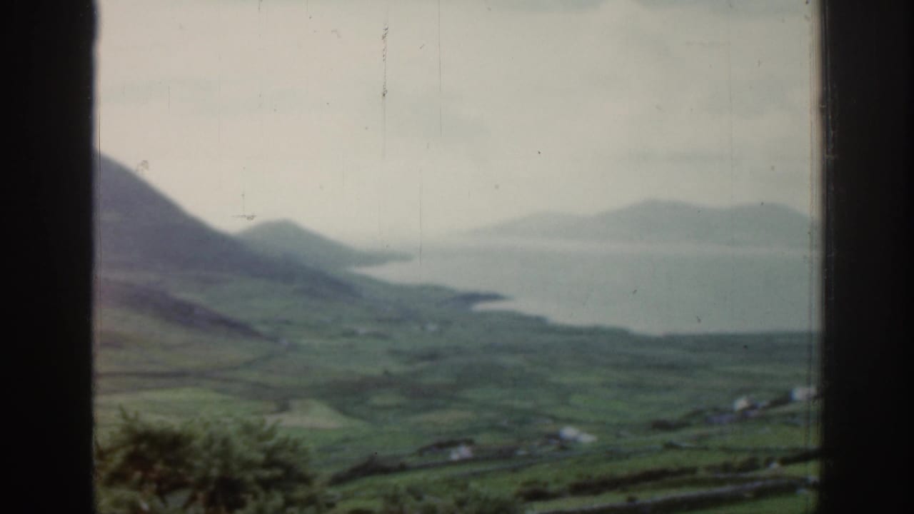 Coastal bay viewed across green hills and distant mountains.