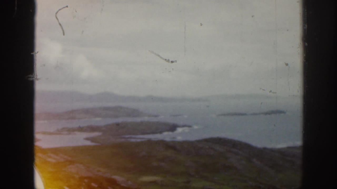 1961 Ireland home-movie view of rolling green hills, coastal inlets, and distant islands under an overcast sky.