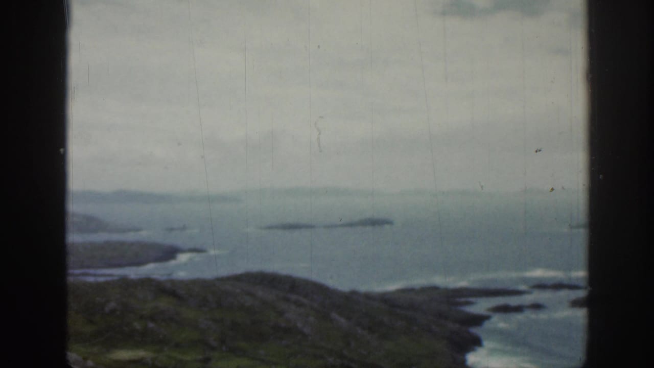 1961 Ireland 8mm frame showing a window-framed coastal panorama with green hills in the foreground and small islands across the water.