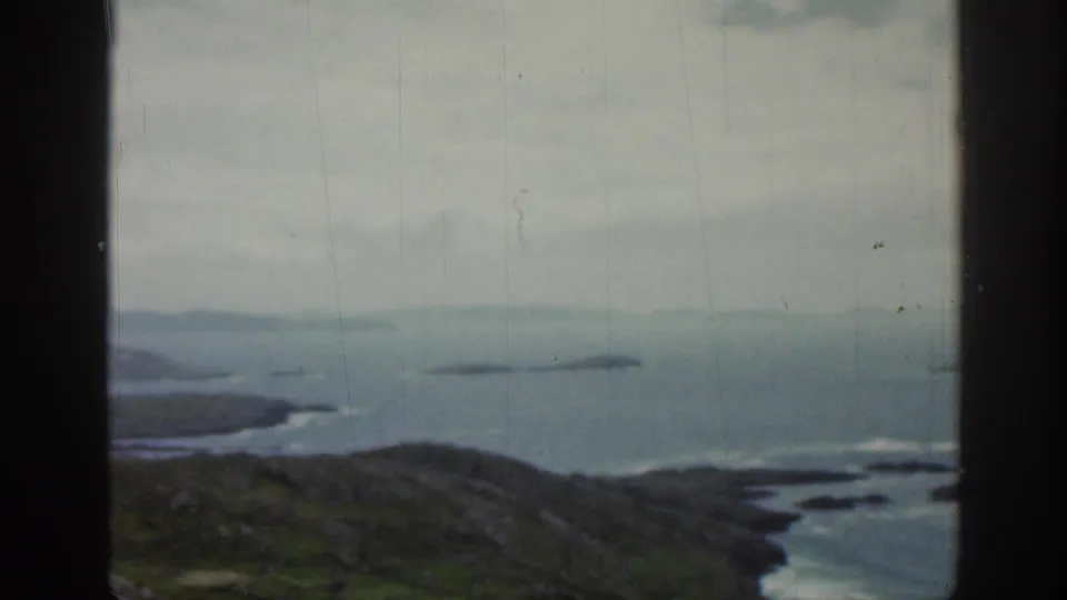 1961 Ireland 8mm frame showing a window-framed coastal panorama with green hills in the foreground and small islands across the water.