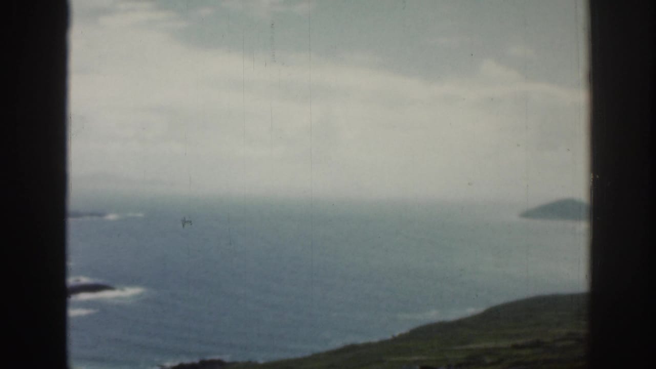 Ocean horizon, coastal slope, and distant island shape seen past a window frame.