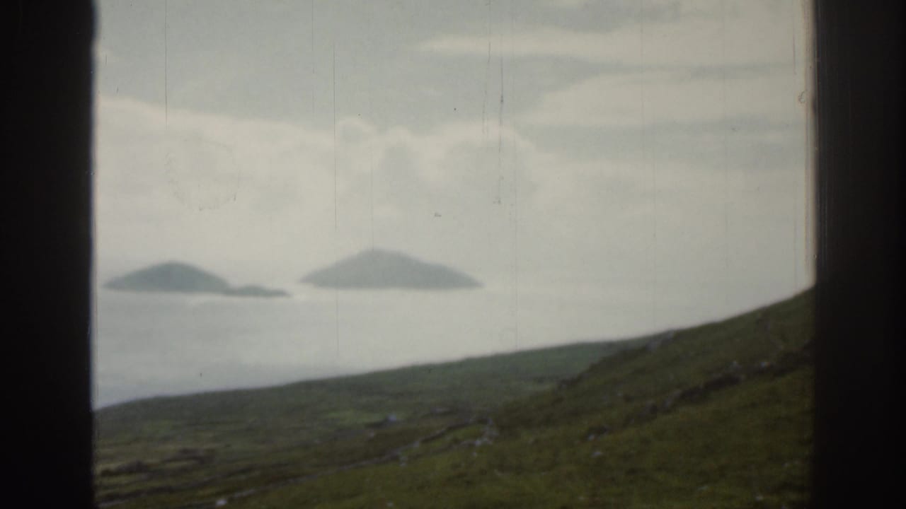 Two distant islands beyond a green slope, divided by a dark vertical frame.