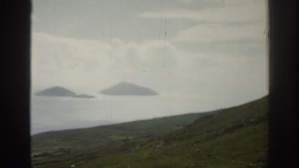 A 1961 Ireland coastal landscape shows two low islands beyond water, with a dark window frame splitting the view.