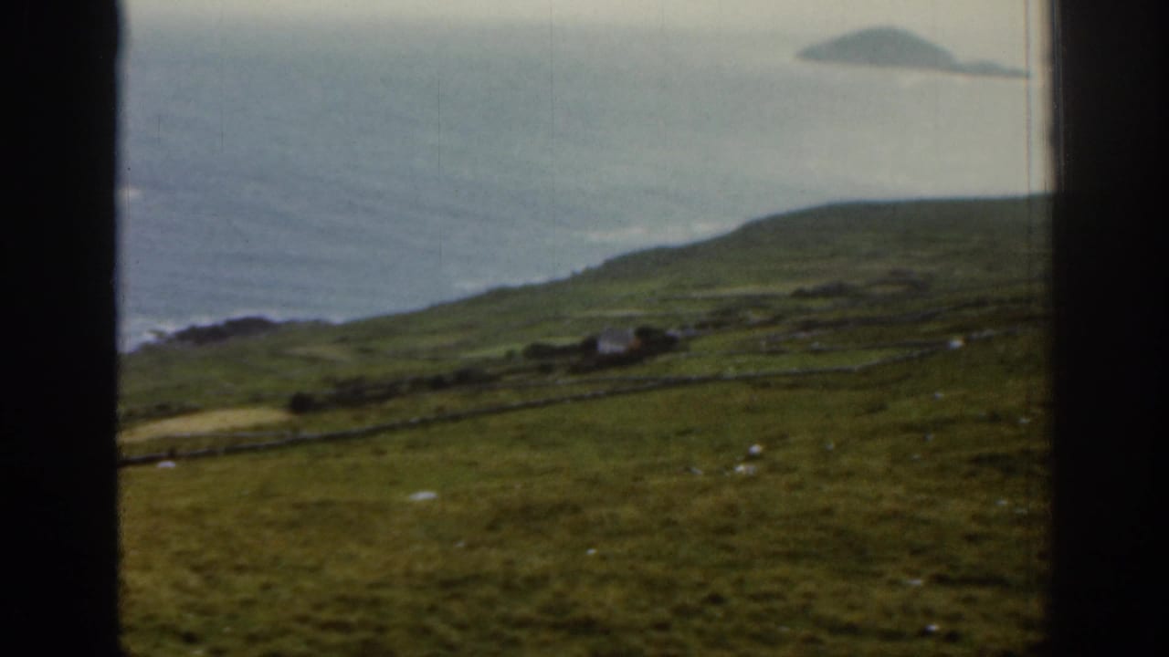Coastal green hillside with stone-walled fields, ocean, and a distant island.
