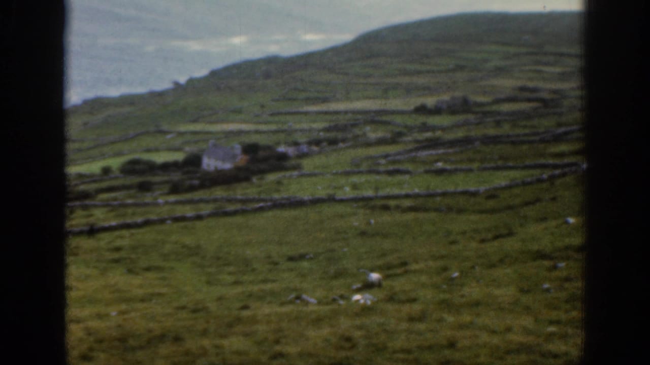 1961 Ireland frame of a rural hillside, stone-walled fields, scattered cottages, and the ocean beyond under hazy light.