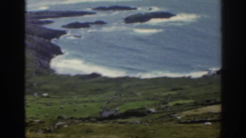 1961 Ireland 8mm coastal view showing a blue bay, rocky headland, small islands, and pale surf along the shore.