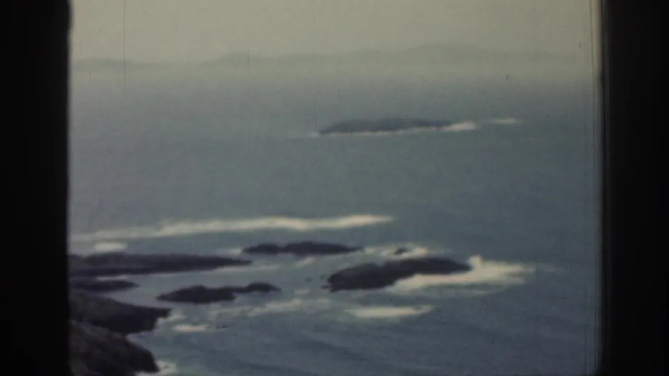 1961 Ireland coastal frame with rocky outcrops, breaking waves, and a soft horizon divided by a window frame.