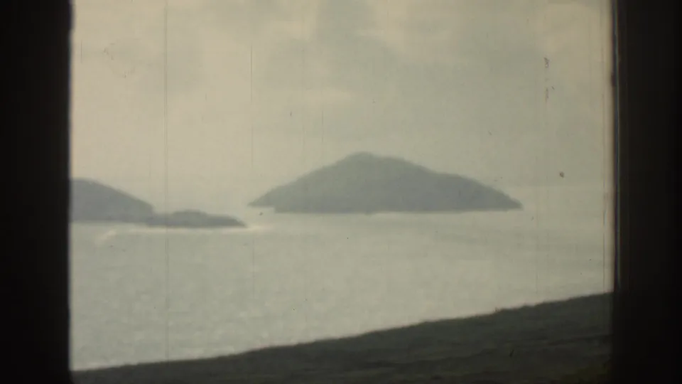 1961 Ireland 8mm frame showing distant island shapes across pale water with a dark foreground slope.