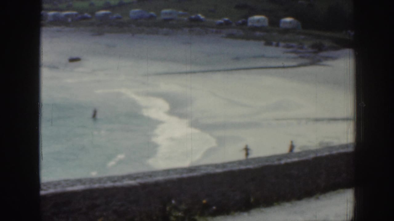 Shallow tidal water and exposed sand with distant walkers, framed by dark vertical and horizontal window edges.