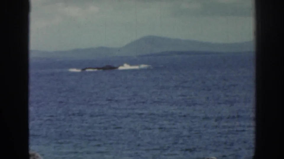 1961 Ireland 8mm frame showing open water, far-off surf, hazy hills, and dark window bars cutting through the view.