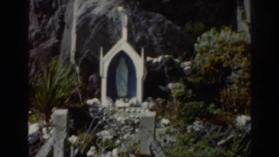A small white shrine or memorial with an arched niche and statue stands among rocks and greenery in the Ireland travel footage.
