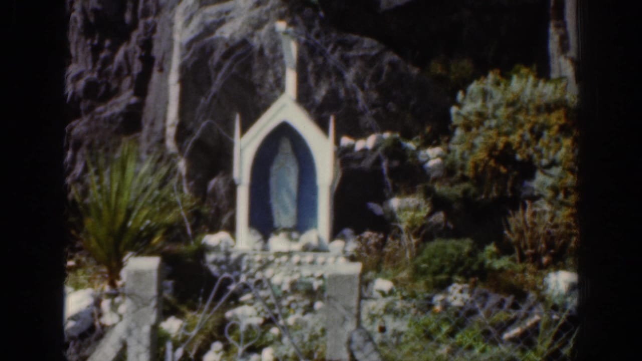 Small white shrine with a blue figure set against rocks and greenery.