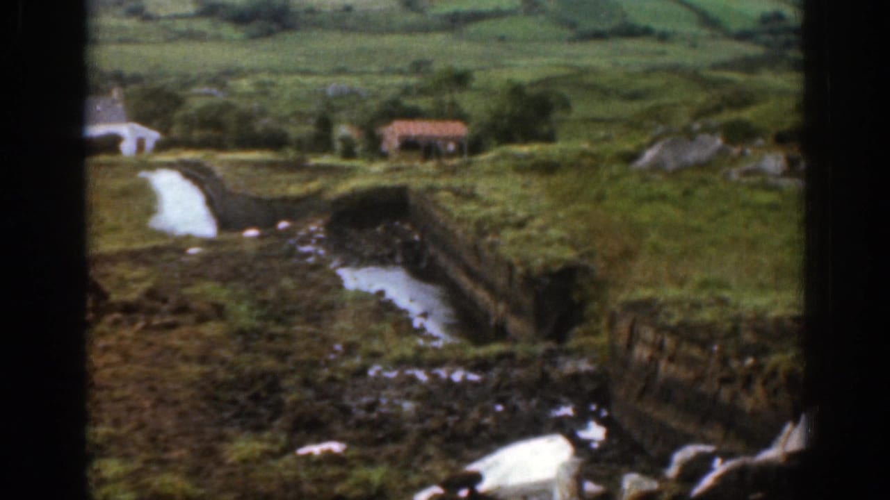 1961 Ireland countryside view showing a winding stream between green banks, with a small distant cottage and low hills beyond.