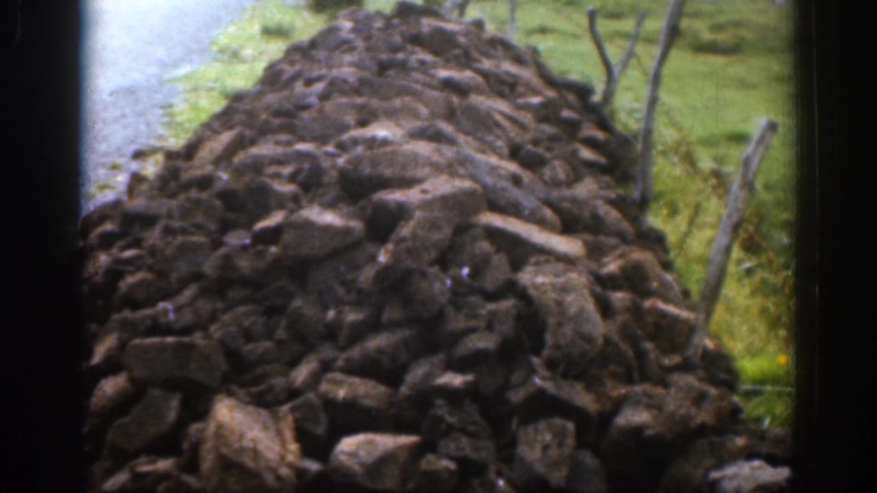 Close view of an Irish dry-stone wall in 1961, showing rough stacked rocks beside grass and simple fence posts.