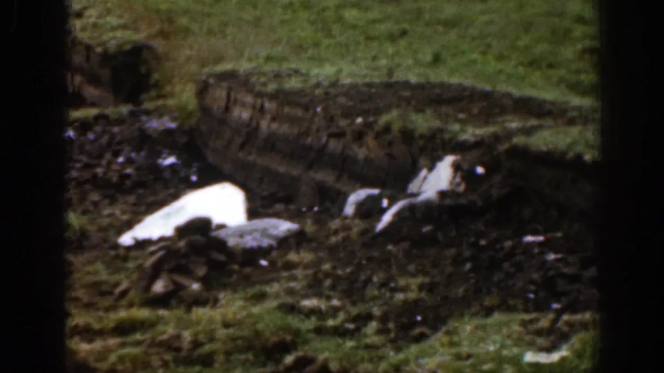 1961 Ireland 8mm view of a muddy rural patch with melting snow or ice, stones, grass, and a weathered bank at the rear.