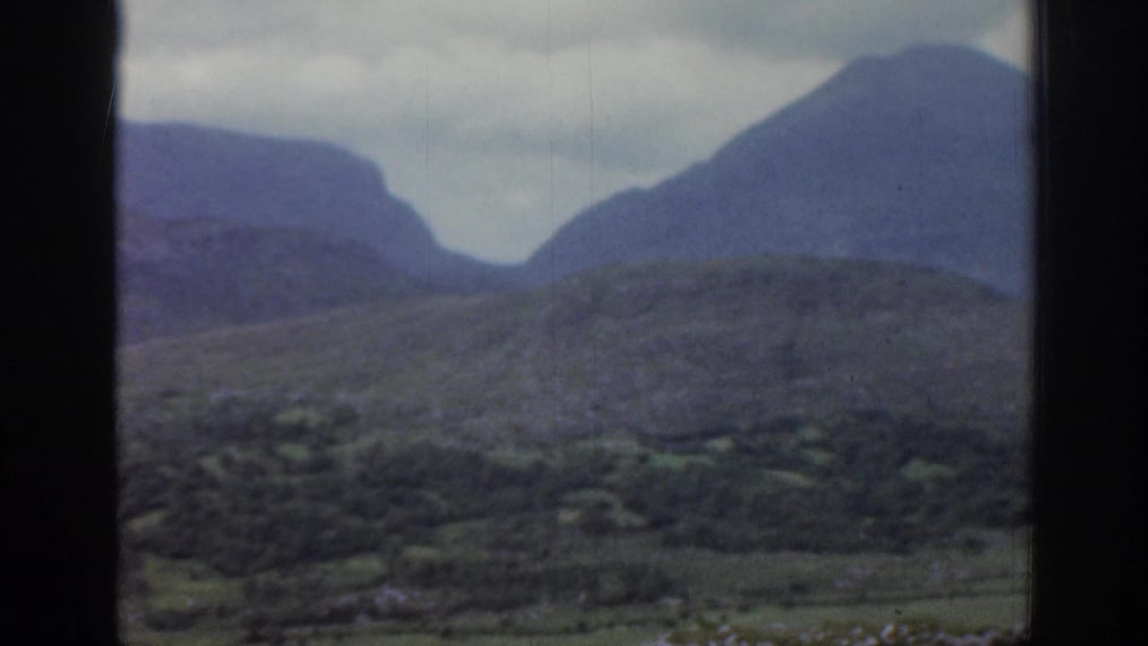 Rugged green hillside with distant mountains under gray cloud.
