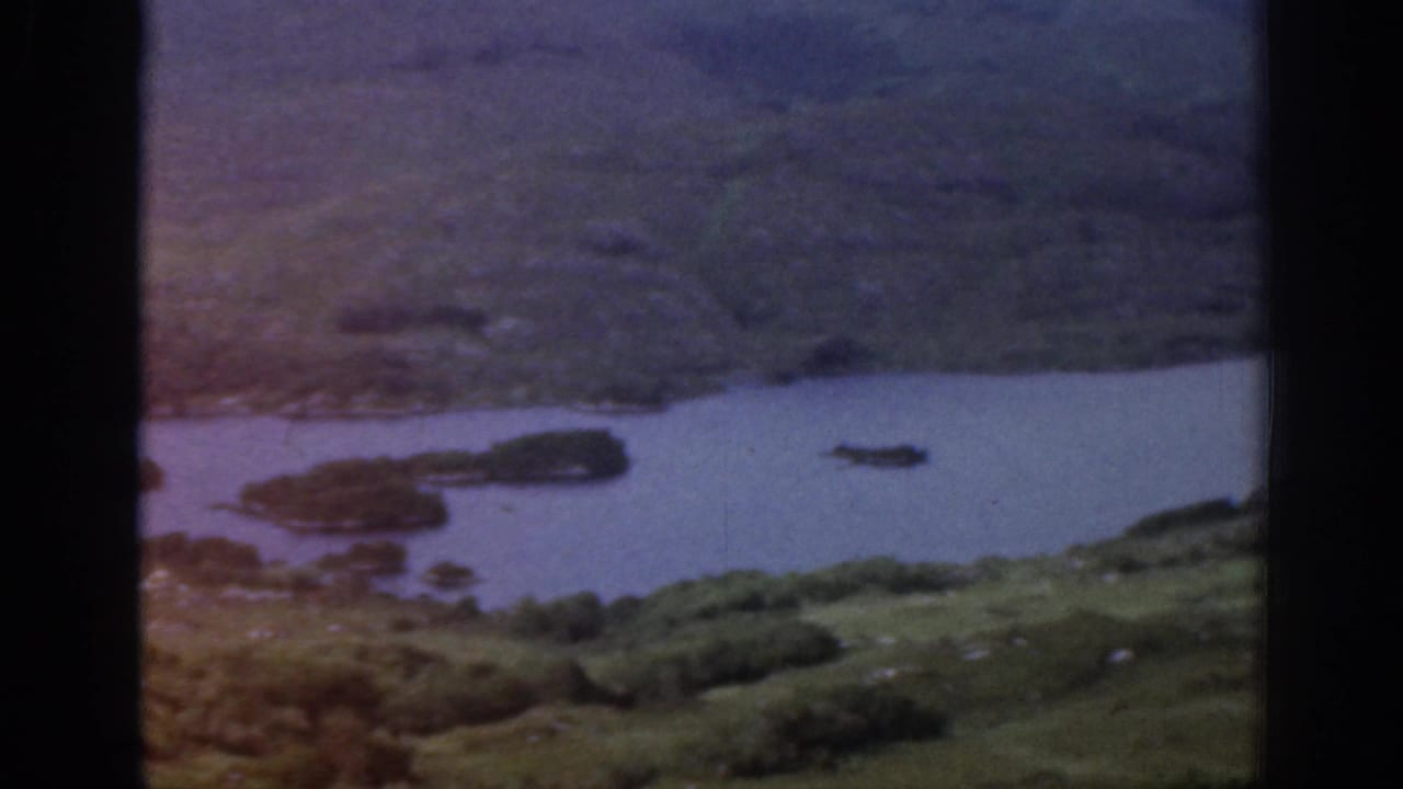 1961 Ireland frame with muted color showing water, small islands, scrubby green slopes, and visible film exposure variation.