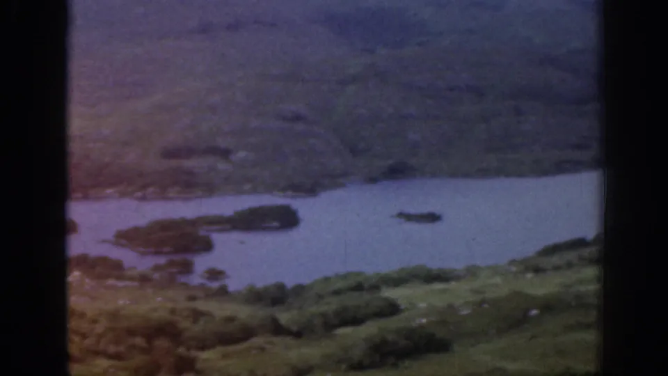 1961 Ireland frame with muted color showing water, small islands, scrubby green slopes, and visible film exposure variation.