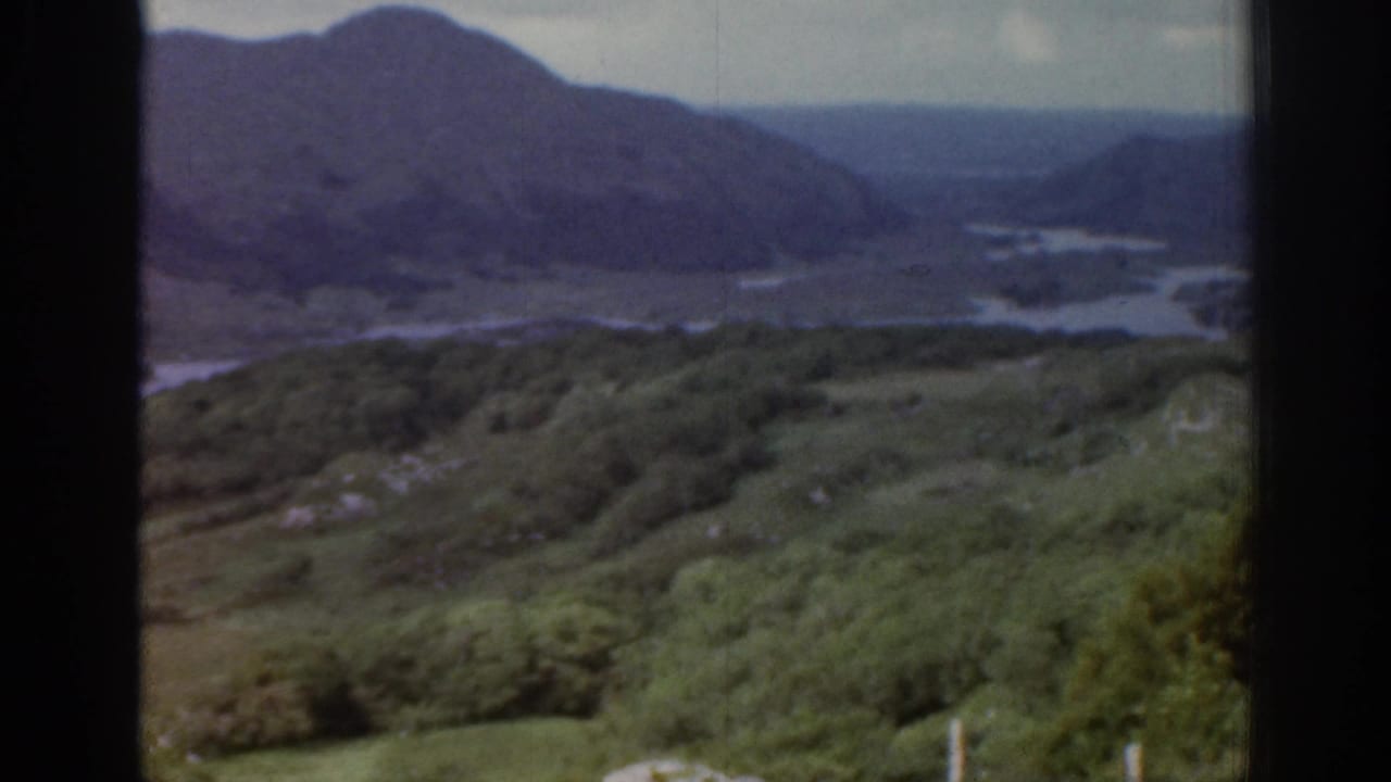 Wider 1961 Ireland landscape view with green hillside vegetation, dark water, and mountains receding into the distance.