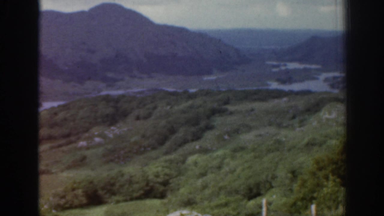 Distant mountain valley with water channels, green slopes and dark film borders.
