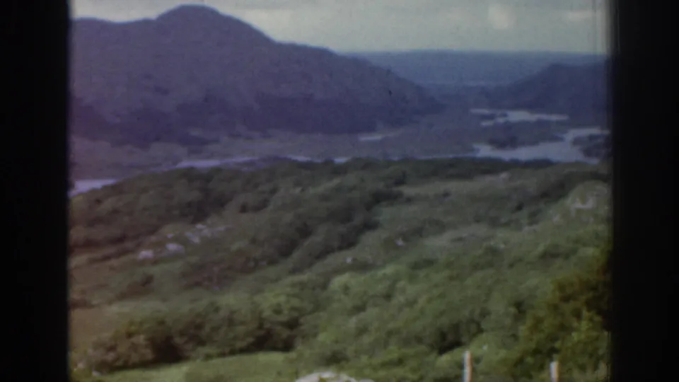 1961 Ireland 8mm frame of a mountain valley, green foreground slopes and winding water in soft focus.