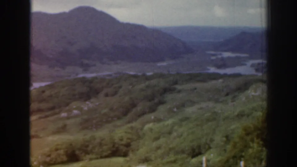 Faded 8mm view from Ireland in 1961 showing hillside vegetation, distant mountains and water below.