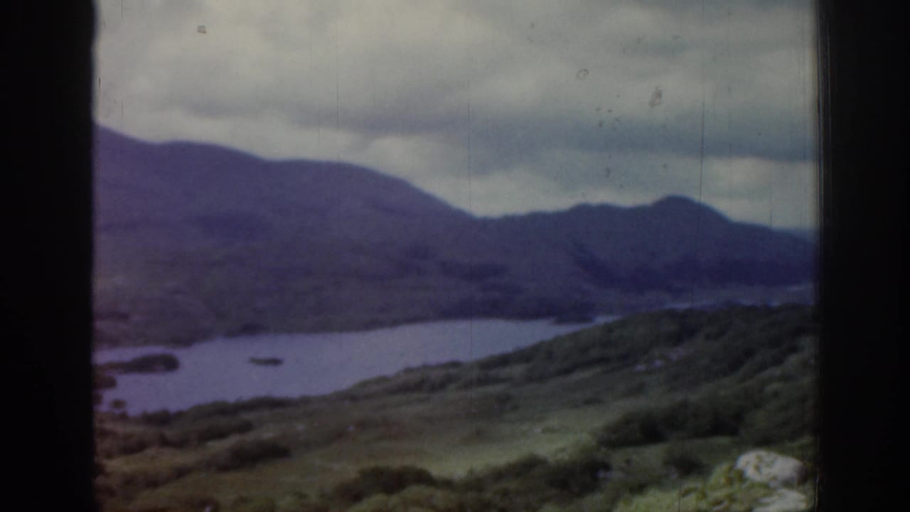 Lake and mountain landscape seen through dark vertical frame edges under heavy clouds.