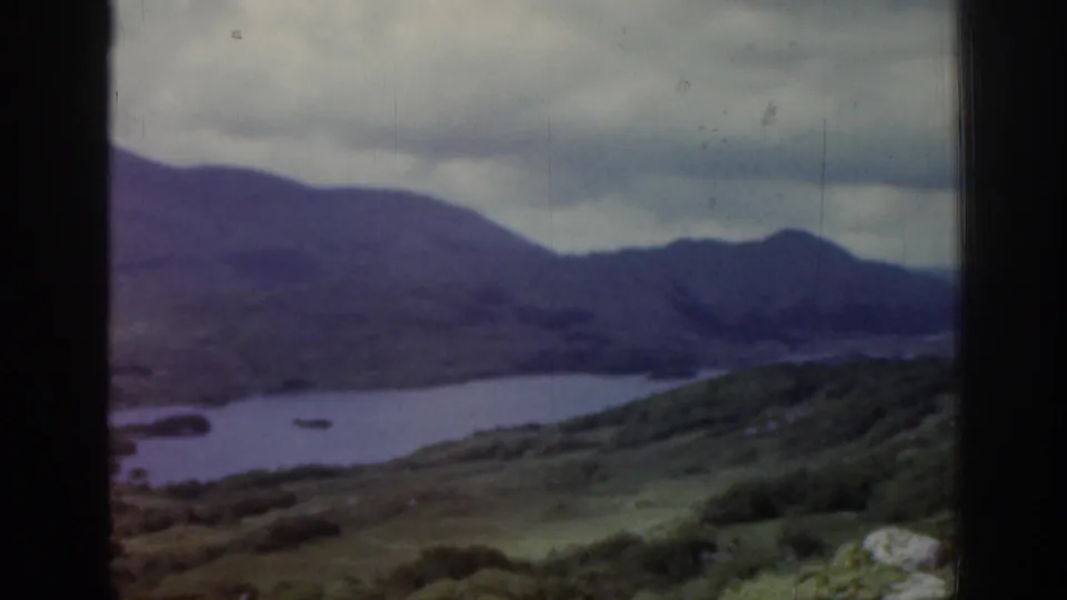 1961 Ireland 8mm frame of a lake below rolling hills and mountains, partially framed by dark window or vehicle edges.